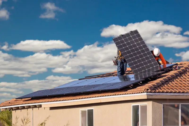 Imagen de un tejado de una casa y dos hombres instalando placas solares